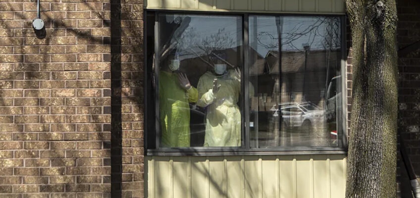 Staff members stand at a window as they watch a parade of well-wishers driving by Orchard Villa Care home, in Pickering, Ontario.