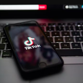 A phone showing the TikTok logo rests on an apple laptop keyboard.