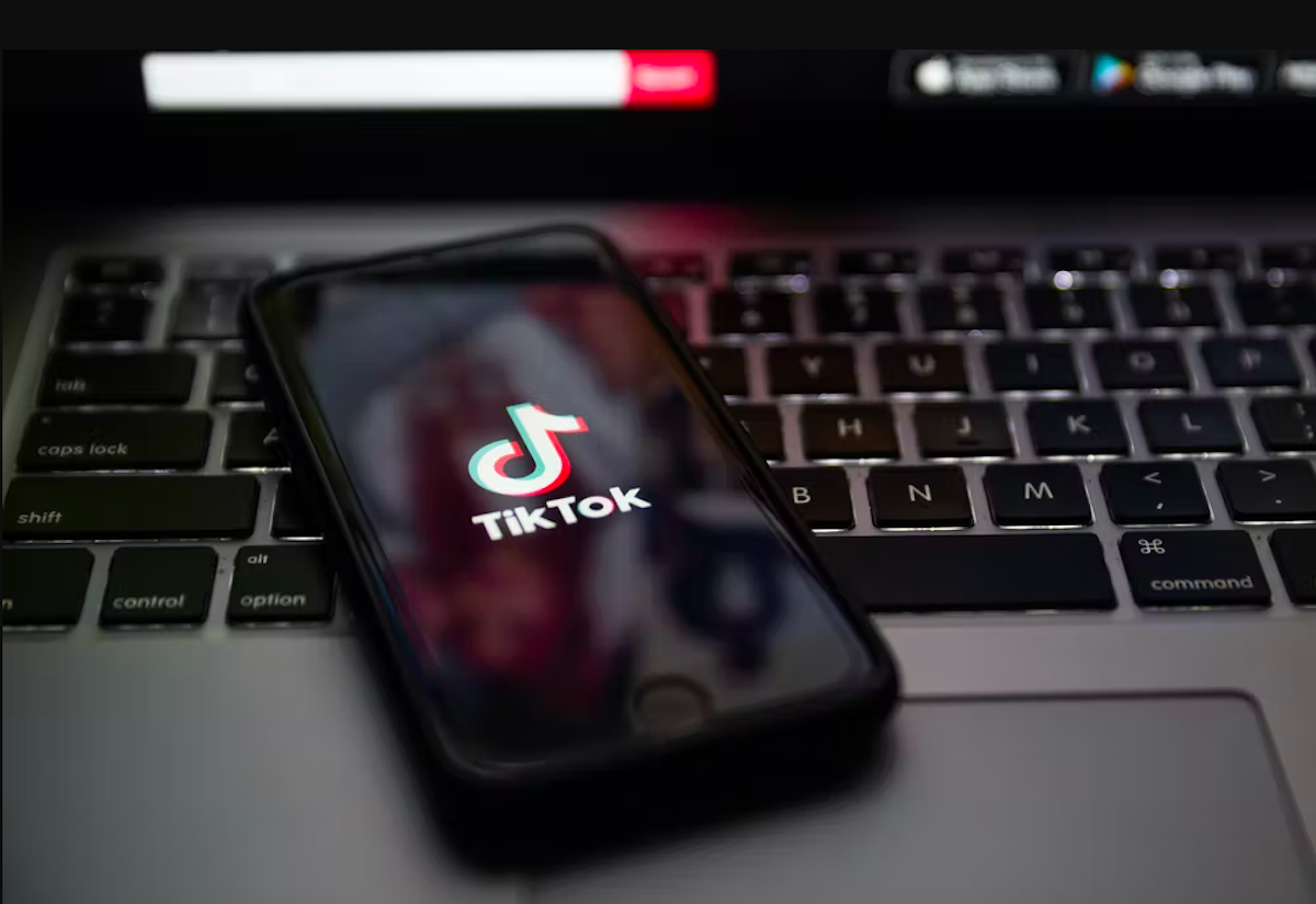 A phone showing the TikTok logo rests on an apple laptop keyboard.