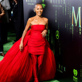 Jada Pinkett Smith smiles wearing an all red outfit in front of a Matrix poster.