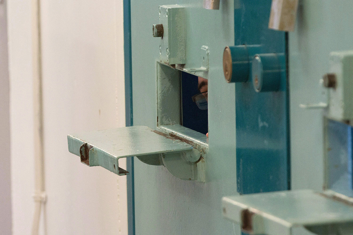 A sliver of the face of an inmate is seen inside a tiny slot in a prison cell door.