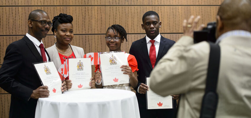 A Black family smiles for a photo while holding their Canadian citizenship certificates.