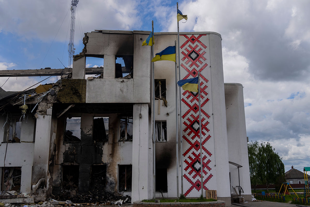 Ukrainian flags flutter outside a destroyed cultural centre with red painted flower decals still visible on one of the walls.