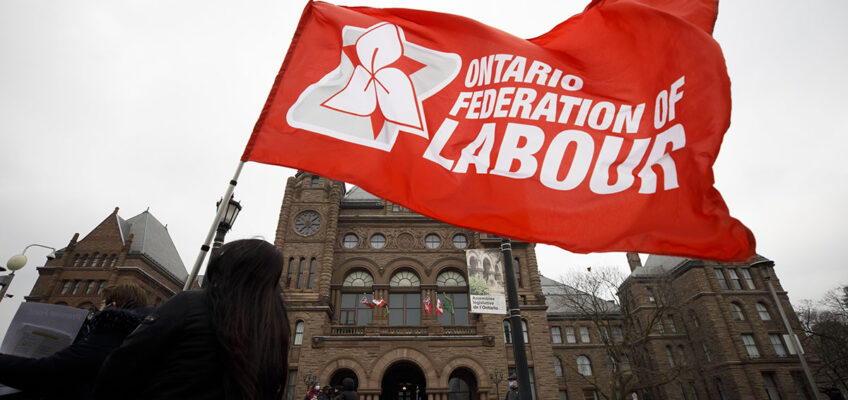 Someone carries a red flag that says 'Ontario Federation of Labour'.