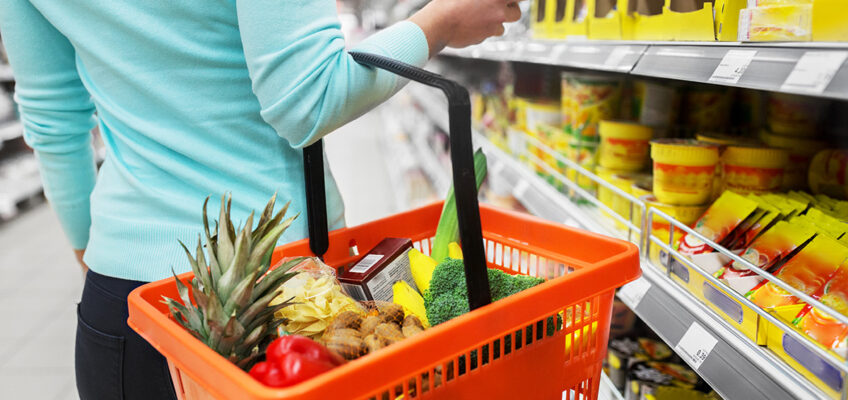 Shopper browsing a shelf in a grocery store with a basket on one arm.