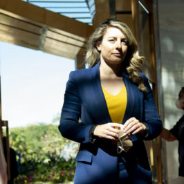 A woman standing wearing a yellow top and a blue blazer.