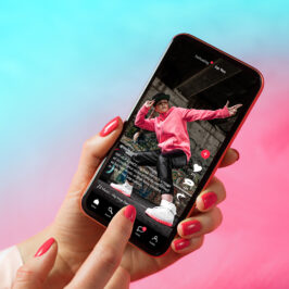 a woman's hand with manicured red nails holds holds a phone showing a person in a dance pose