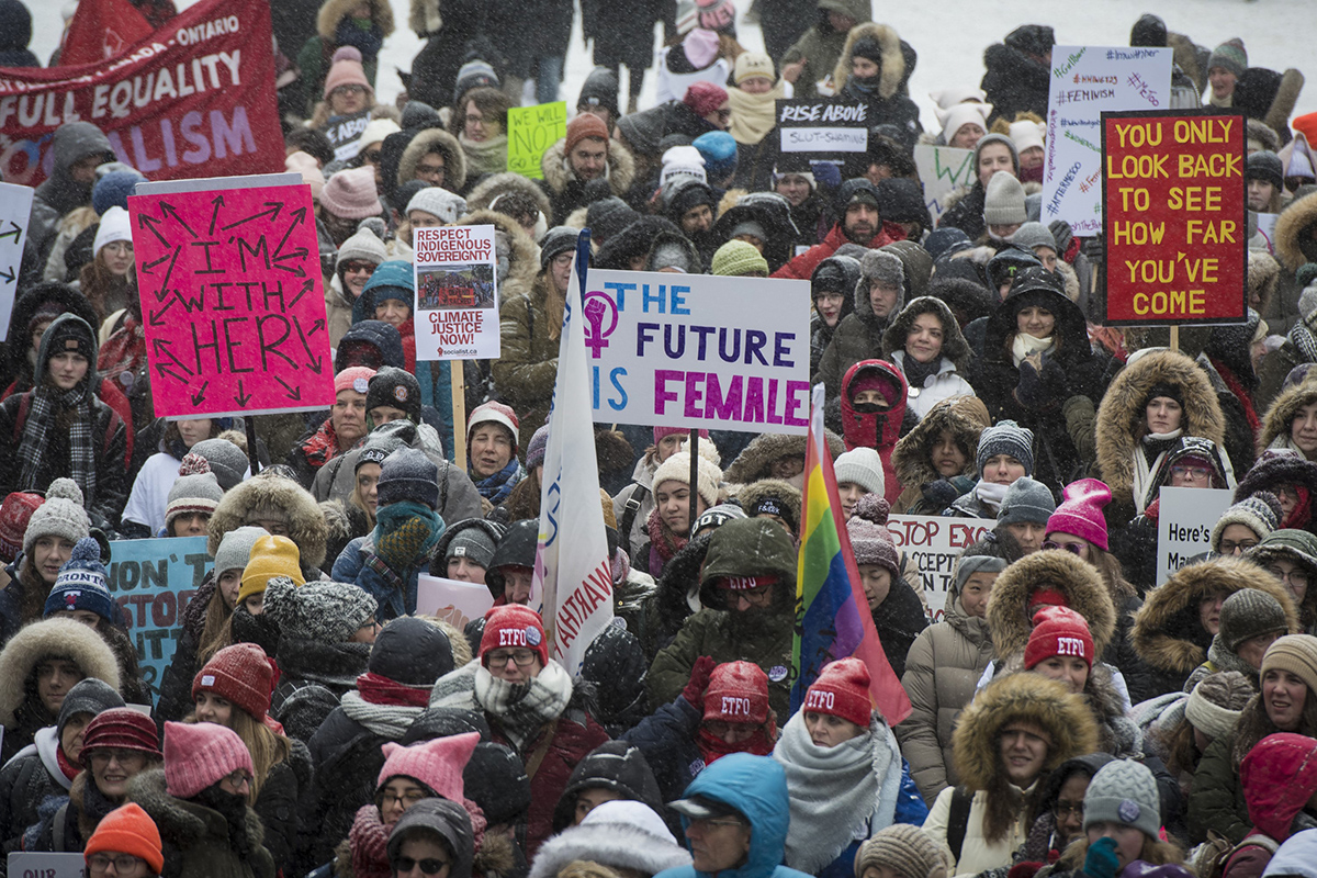 A large crowd gathers, many wearing pink hats. A sign in the middle reads The Future is Female.