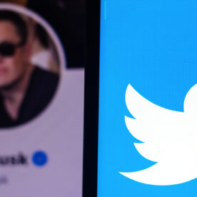 A smartphone with the Twitter logo in the foreground. Behind it is a photo of Elon Musk's Twitter profile.