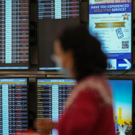 Cancelled flights are seen in red on a digital flight schedules display behind the blurry image of a woman.