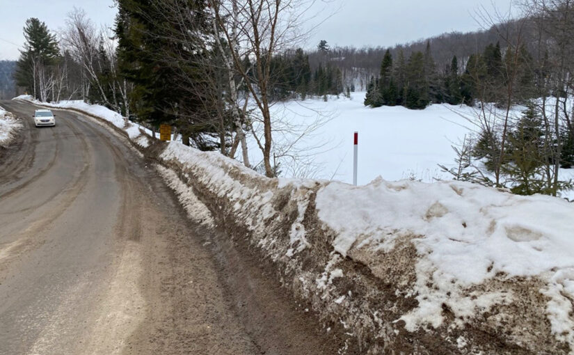 A car drives down a clear road in the winter, with snowbanks on the side of the road.