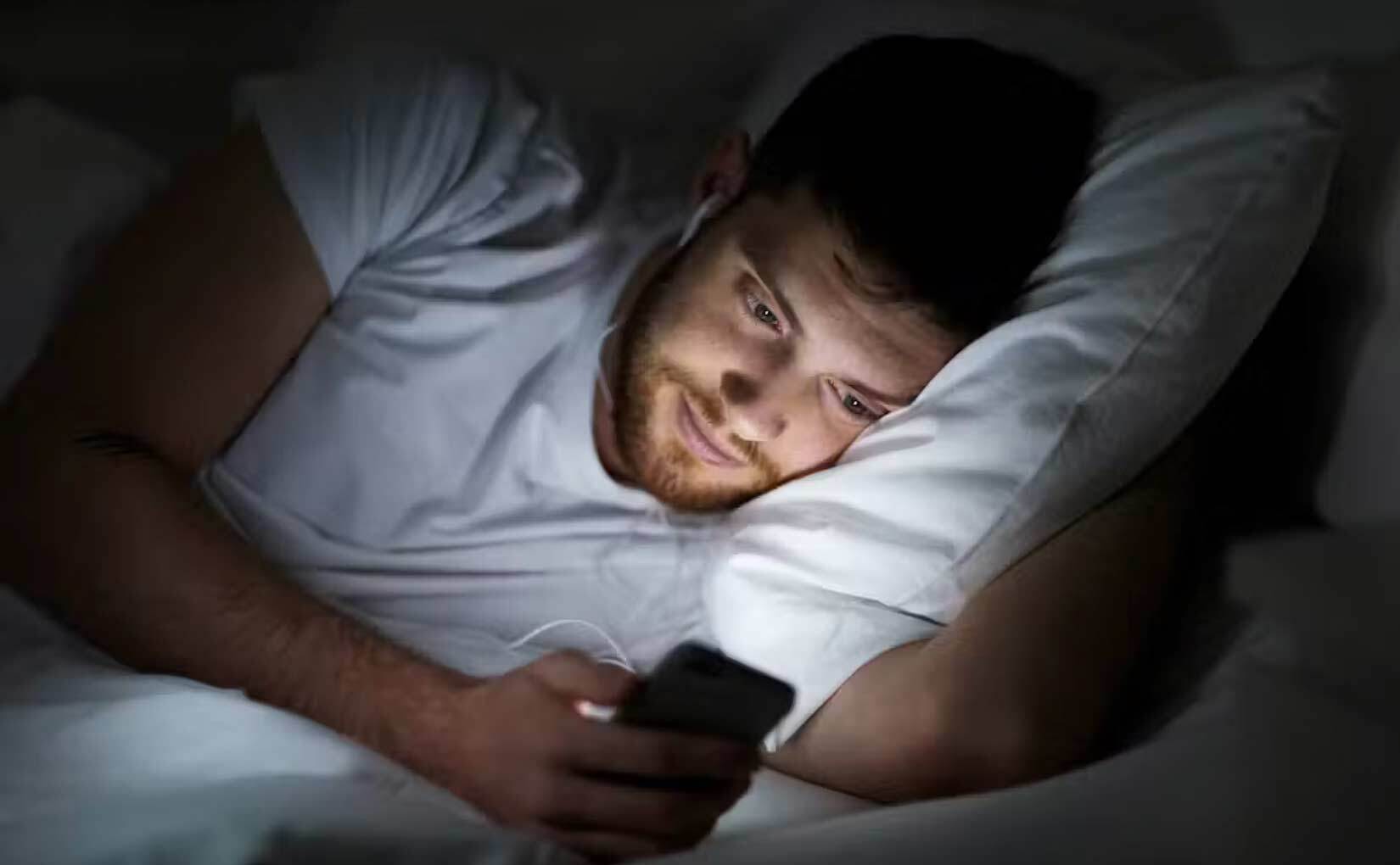 A man looking at a smartphone while lying in bed