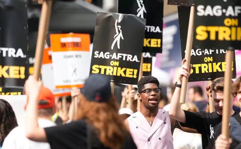 People holding protest signs that say 'SAG-AFTRA on Strike' walk down the sidewalk