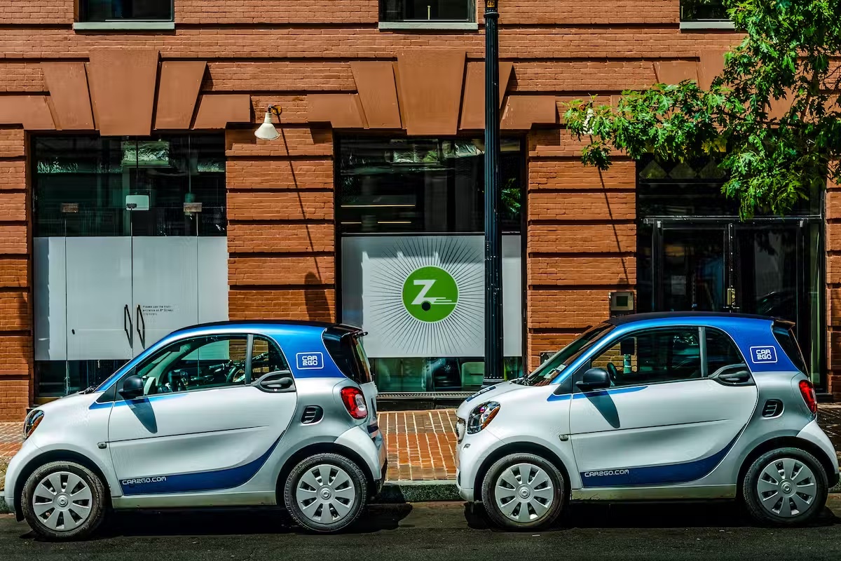 Two small cars parked on the street outside a business with a Zipcar logo posted in the window