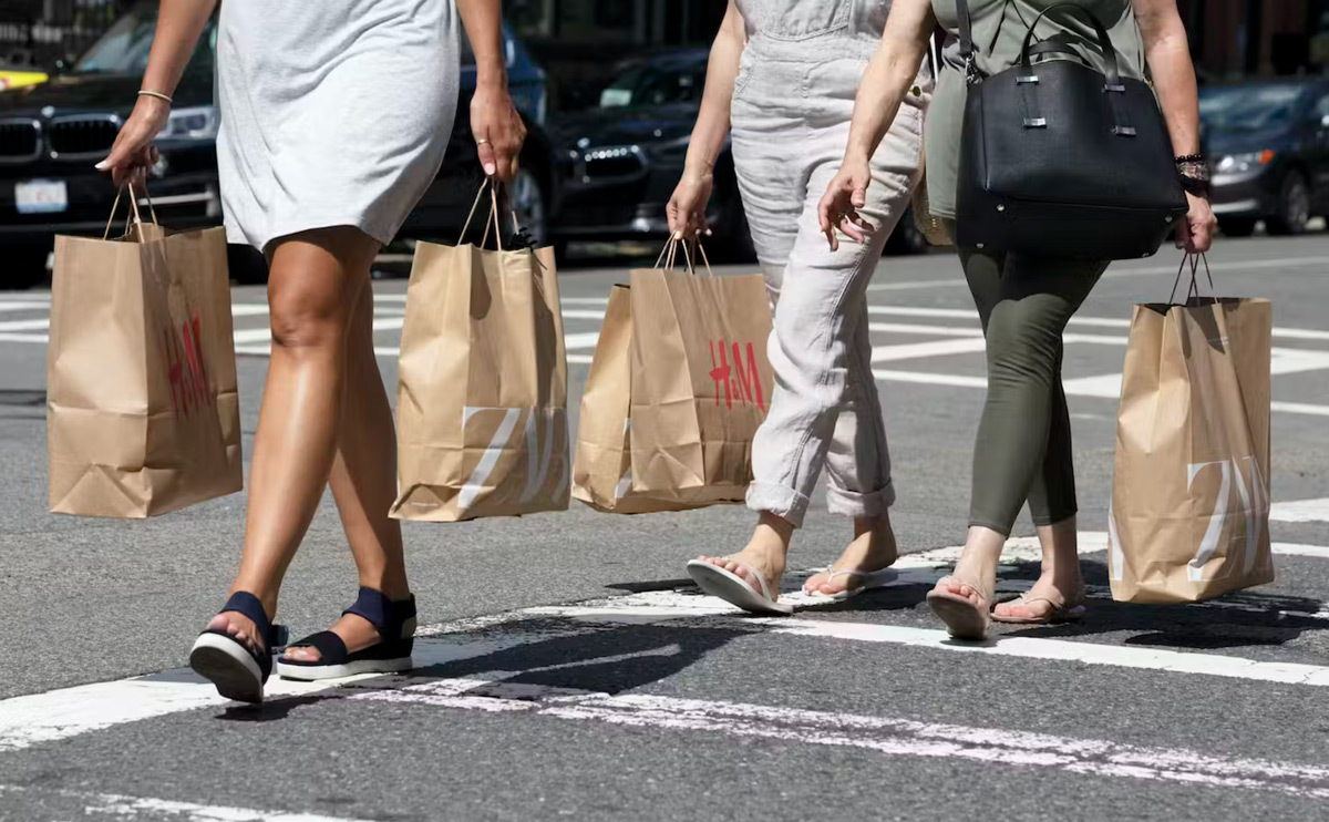 Three people walk on a crosswalk carrying paper shopping bags.