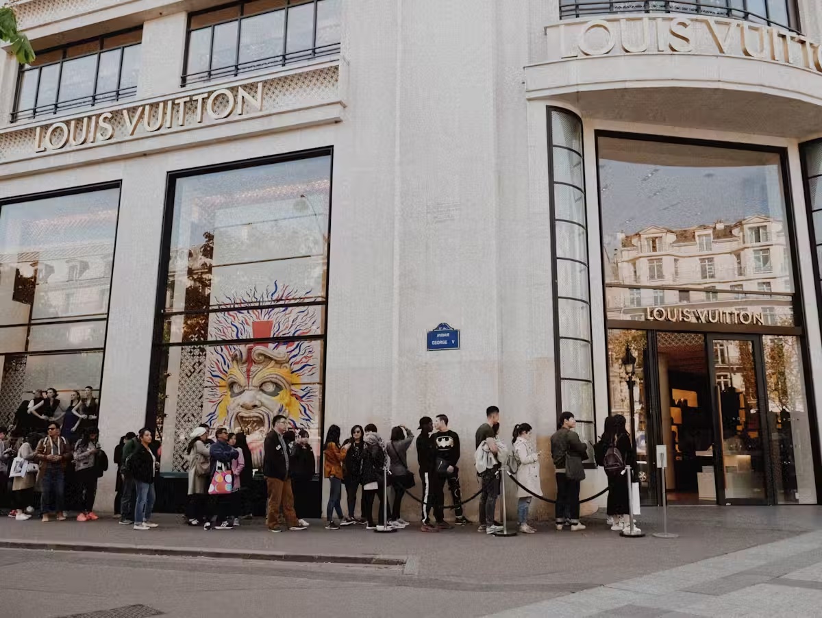A line of people stand outside a Louis Vuitton store.