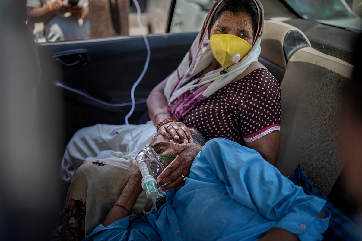 A man wearing an oxygen mask rests his head on a woman's lap. Both are in the backseat of a car.