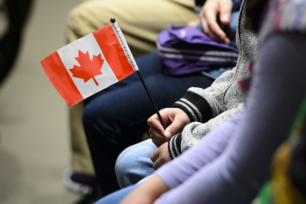 The hands of a person are seen holding a small Canadian flag.