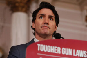 A dark haired man stands behind microphone and a podium that reads 'tougher gun laws'.