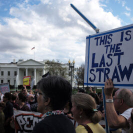 A group of protesters stand outside the White House with placards demanding climate action.