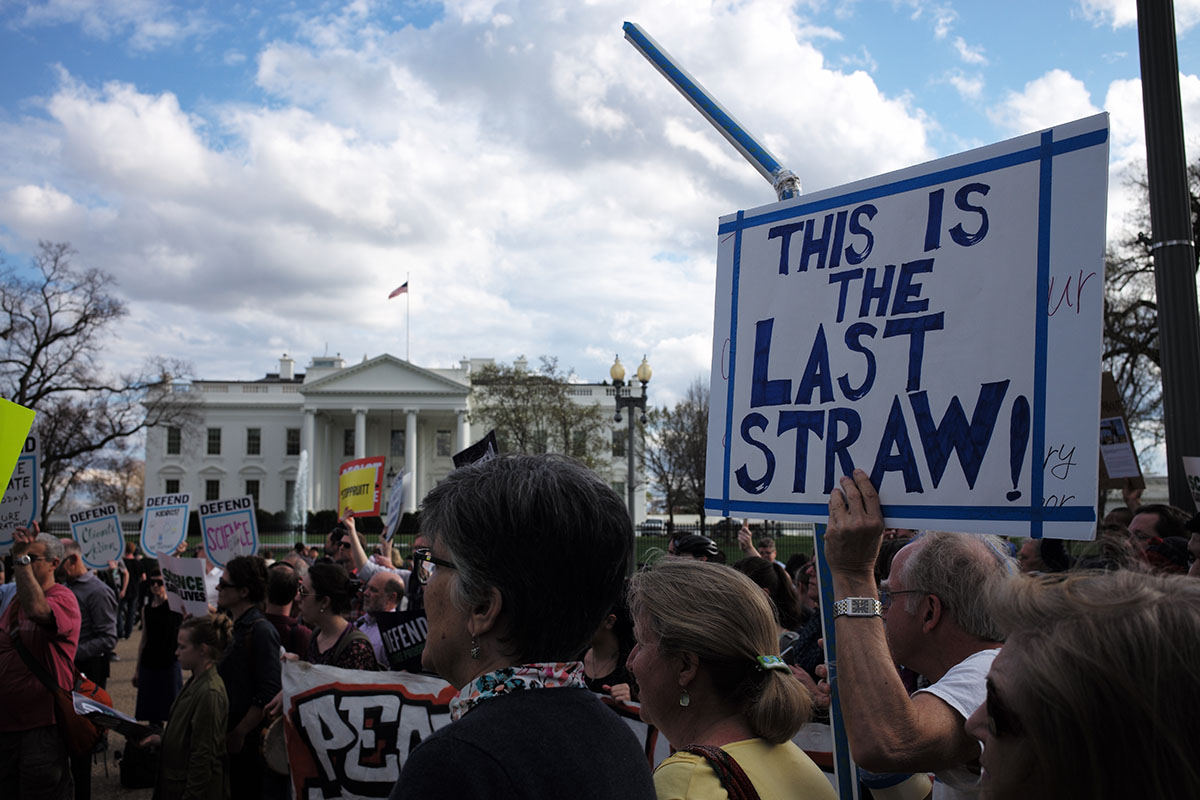A group of protesters stand outside the White House with placards demanding climate action.