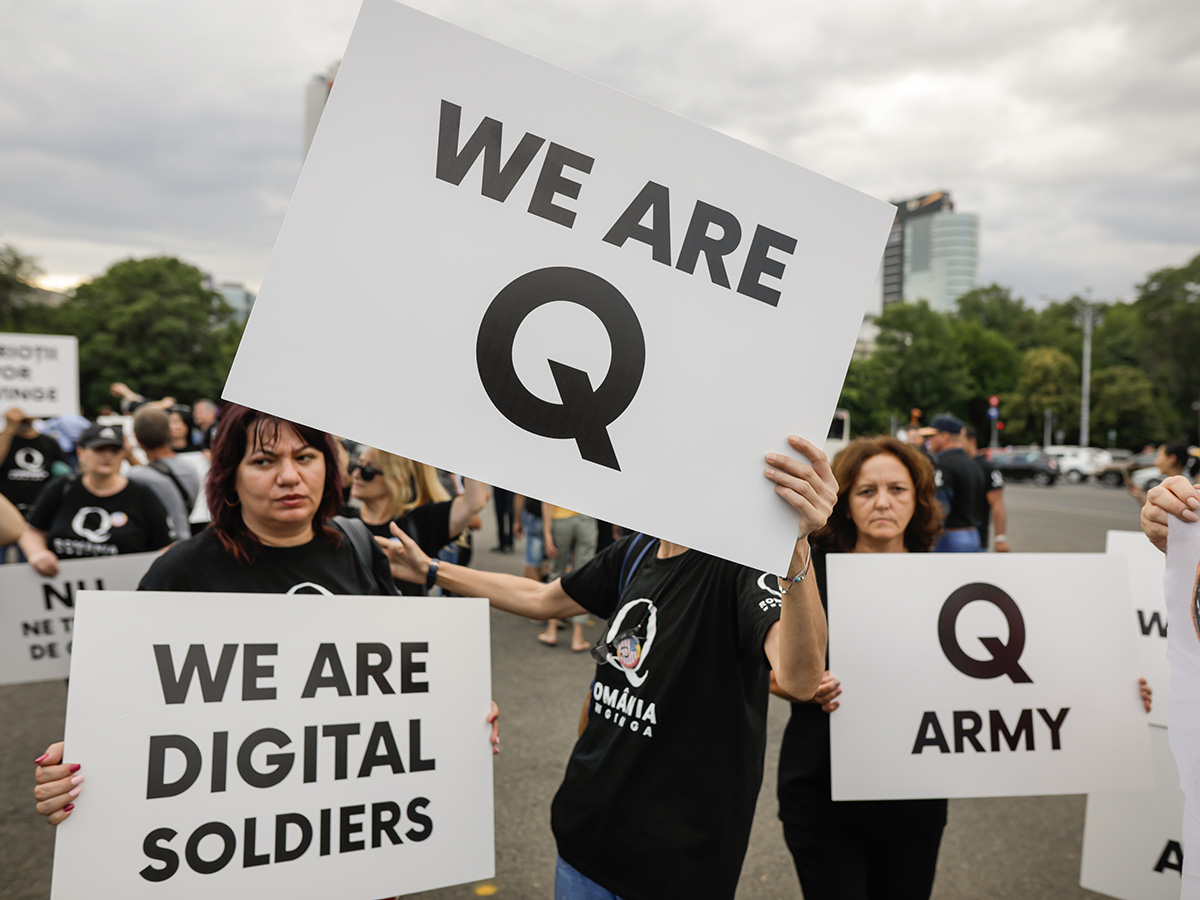 three white women holding signs that read WE ARE Q, Q ARMY and WE ARE DIGITAL SOLDIERS.
