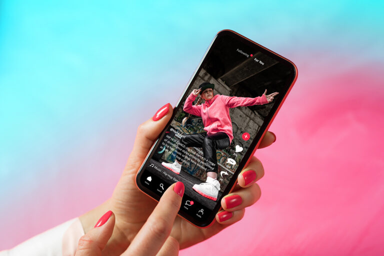 a woman's hand with manicured red nails holds holds a phone showing a person in a dance pose