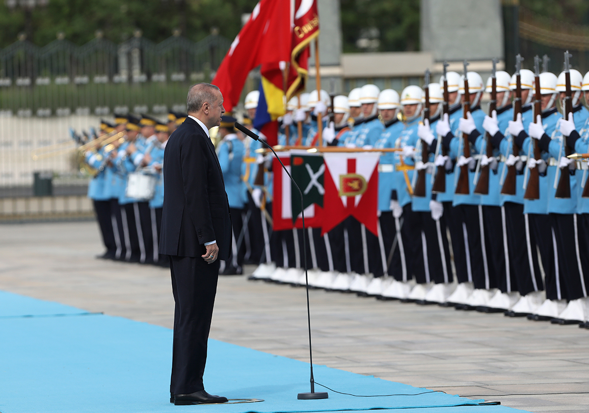 A man in a suit stands on a pale blue carpet looking at a military honour guard dressed in the same shade of blue.