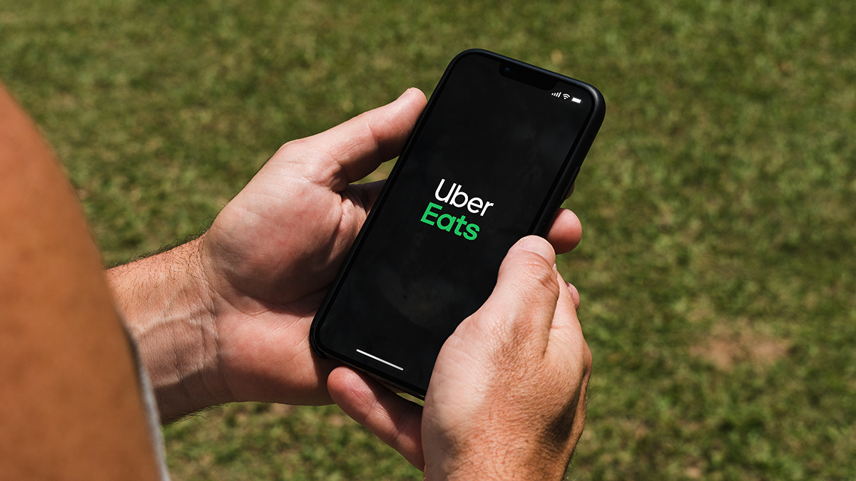 Hands holding a smartphone with the Uber Eats app loading screen visible on it.