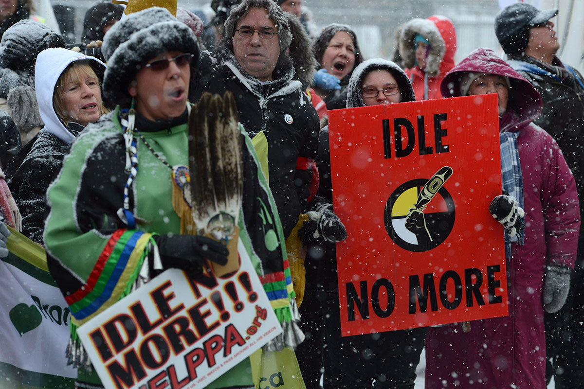 People wearing winter clothing carry signs that read: Idle No More.