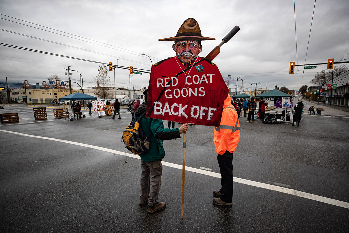 A demonstrator holds a sign with a caricature of an RCMP officer.