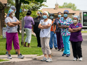 A group of women dressed as nurses wearing face masks stand on a roadside.