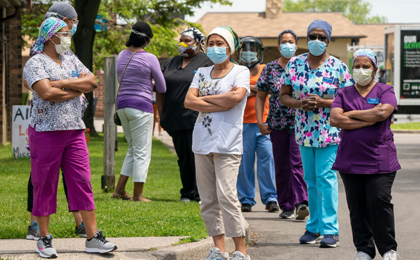 A group of women dressed as nurses wearing face masks stand on a roadside.