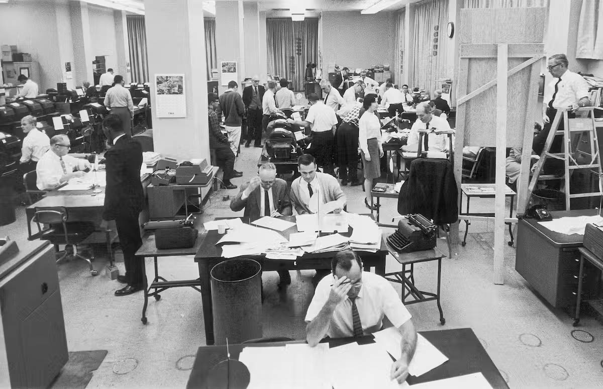 A black-and-white photo of journalists working in a newsroom