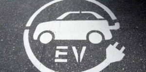 An electric car with "EV" and a cord is drawn in white chalk on the pavement