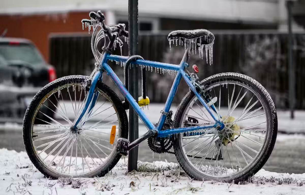 A blue two-wheeled bicycle is locked to a pole outside and is covered in ice.