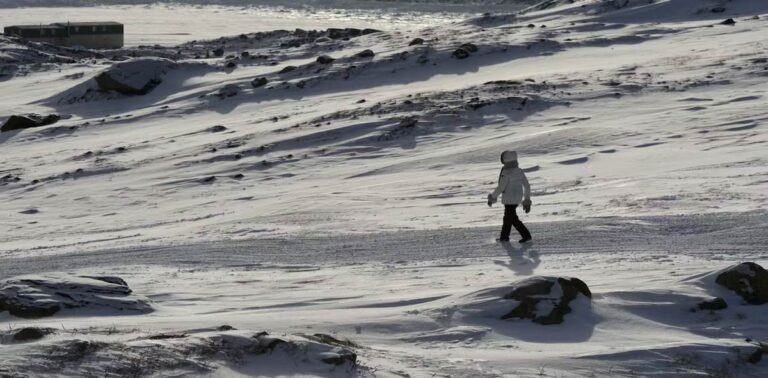 A person in a parka walks across a snowy landscape