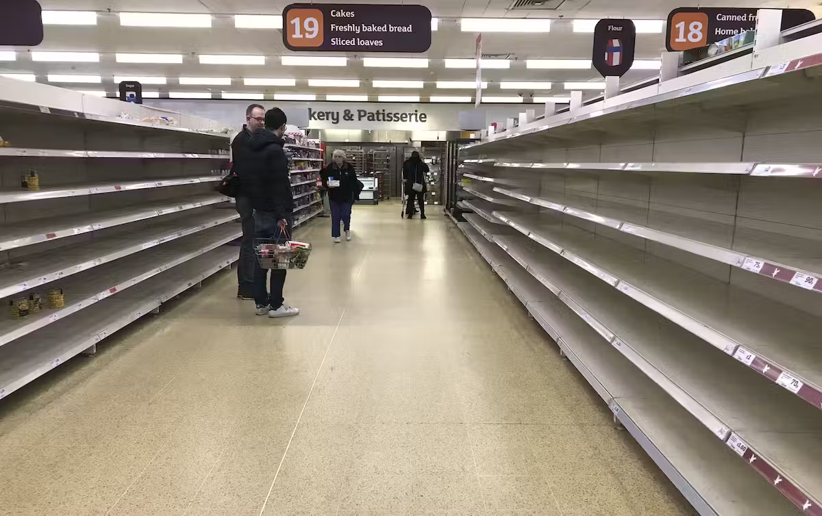 People stand in the middle of a supermarket aisle lined with empty shelves