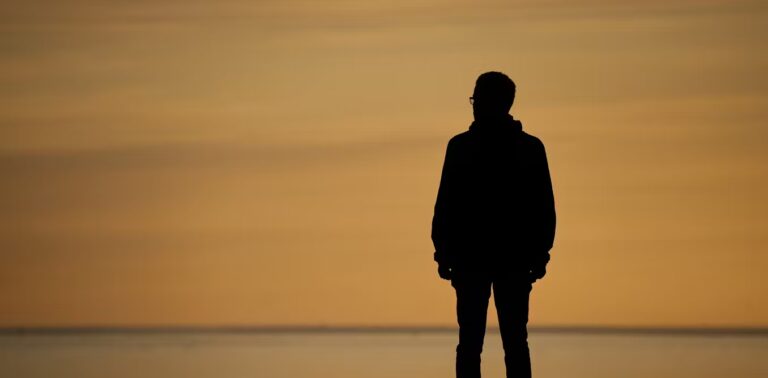 A silhouette of a man looking out at a sunset.