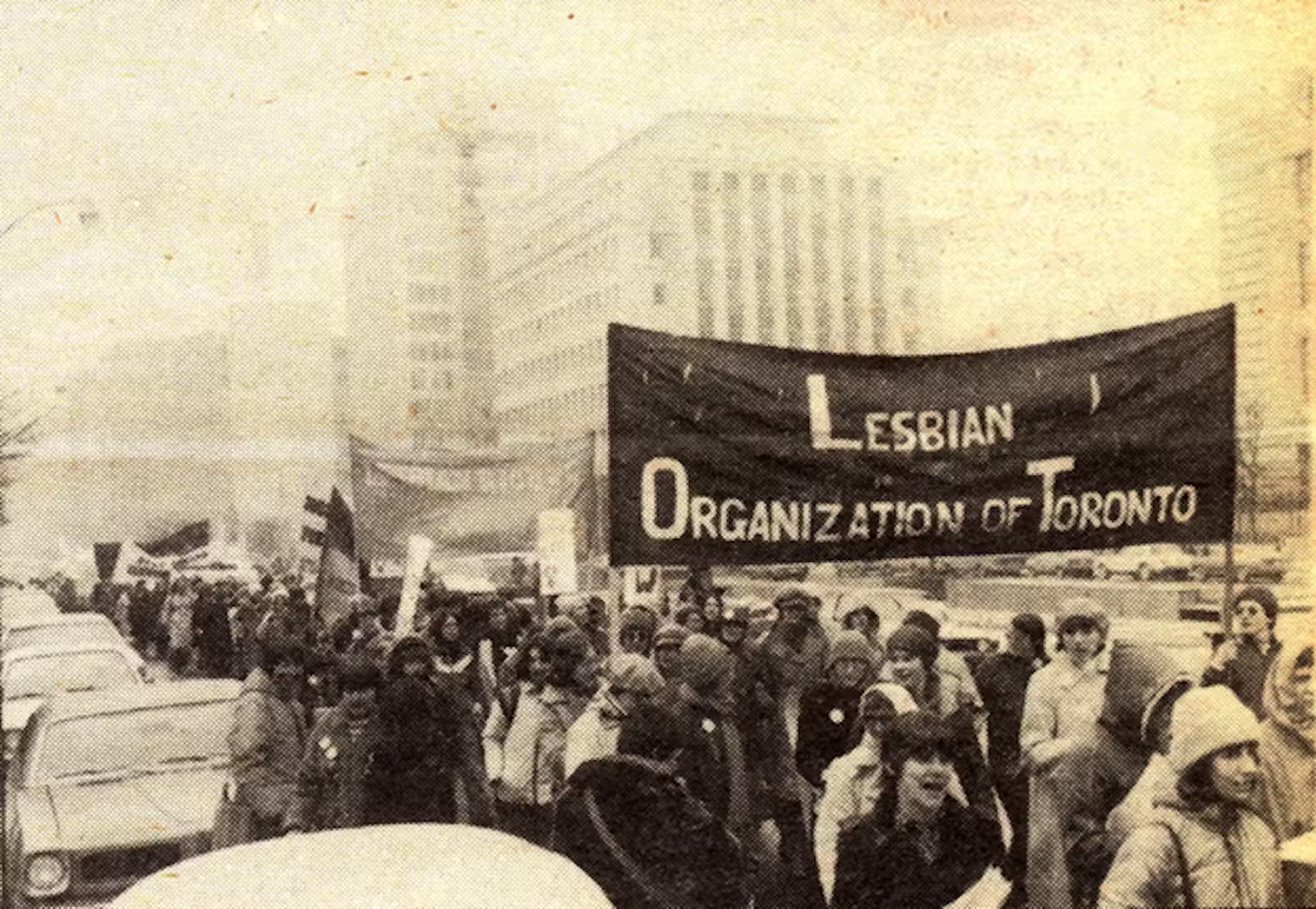 A black and white photo of people at a demonstration carrying a large banner reading: Lesbian organization of Toronto.