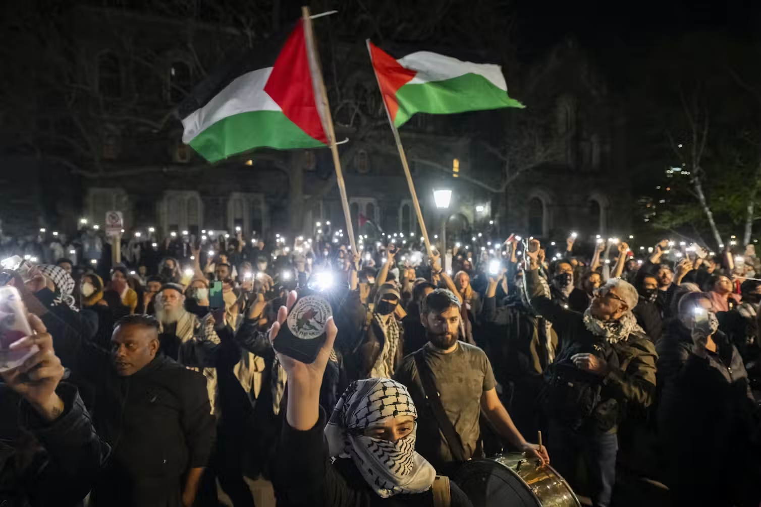 A nighttime protest shows demonstrators waving Palestinian flags.