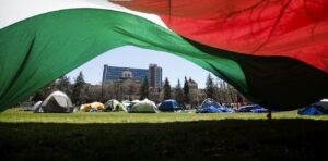 A Palestinian flag waves in front of a tent encampment on a university campus.