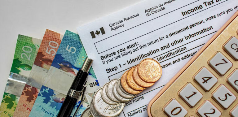 Canadian Tax Forms with coins, calculator, a pen and bills seen on a white table.