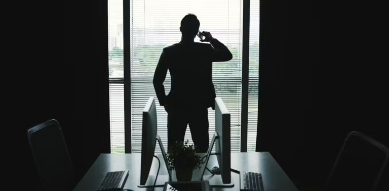 Silhouette of a man in a business suit talking on the phone in an office in front of an open window.
