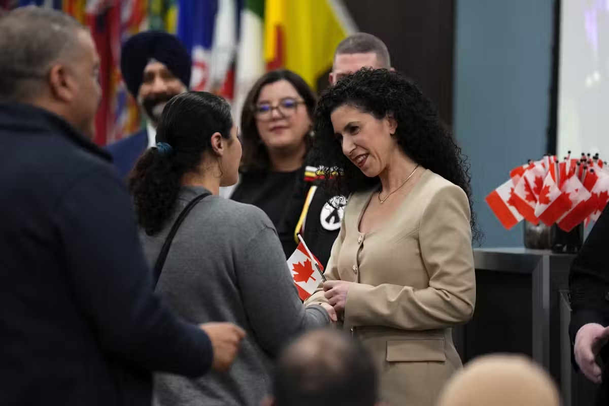 A woman smiles at a couple and hands them a small Canadian flag.