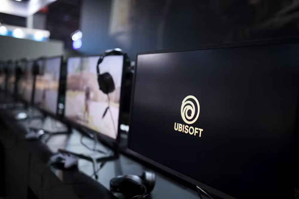 a row of computer screens, one displays the logo of ubisoft and the company's name