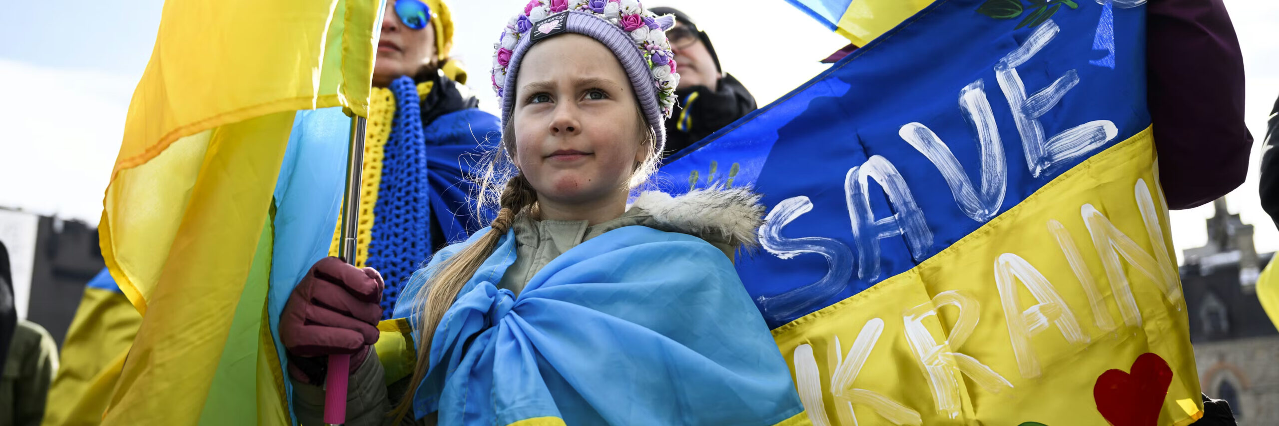 A young girl wrapped in a flag and holding another during a protest.